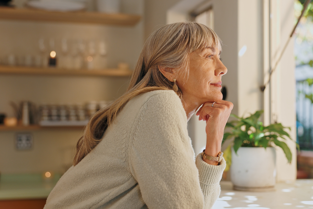 A white woman with grey hair, who is about 60 years old, is looking out of a window.