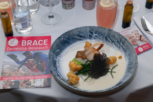 A table with a formal fish dish, BRACE leaflets and drinks.