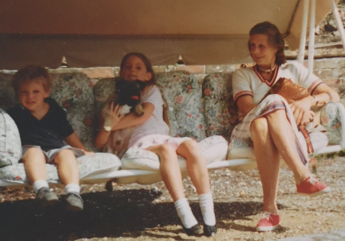 Laura and her brother as children, sat on a swing chair with their granny.