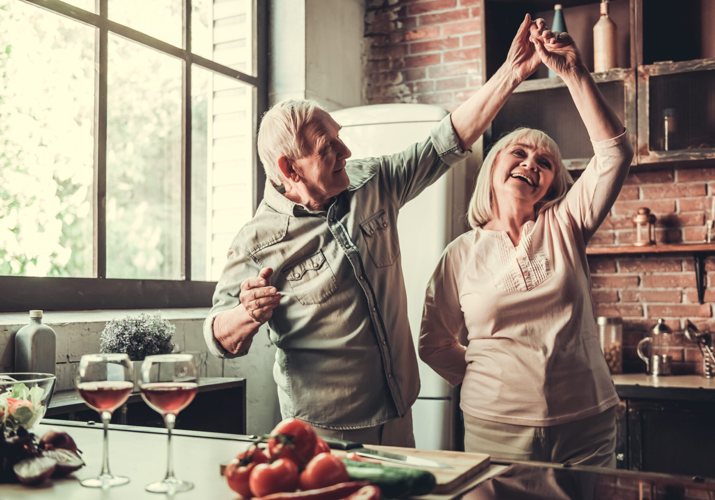An older couple are dancing in their kitchen.