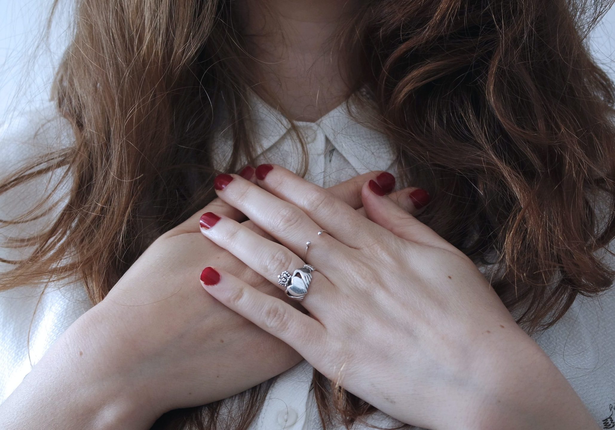 A woman has her hands crossed ove her heart/chest area.